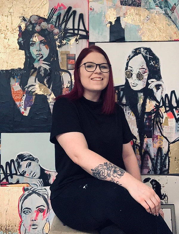 girl sitting in front of her painings that are portraits black and white and with pops of color